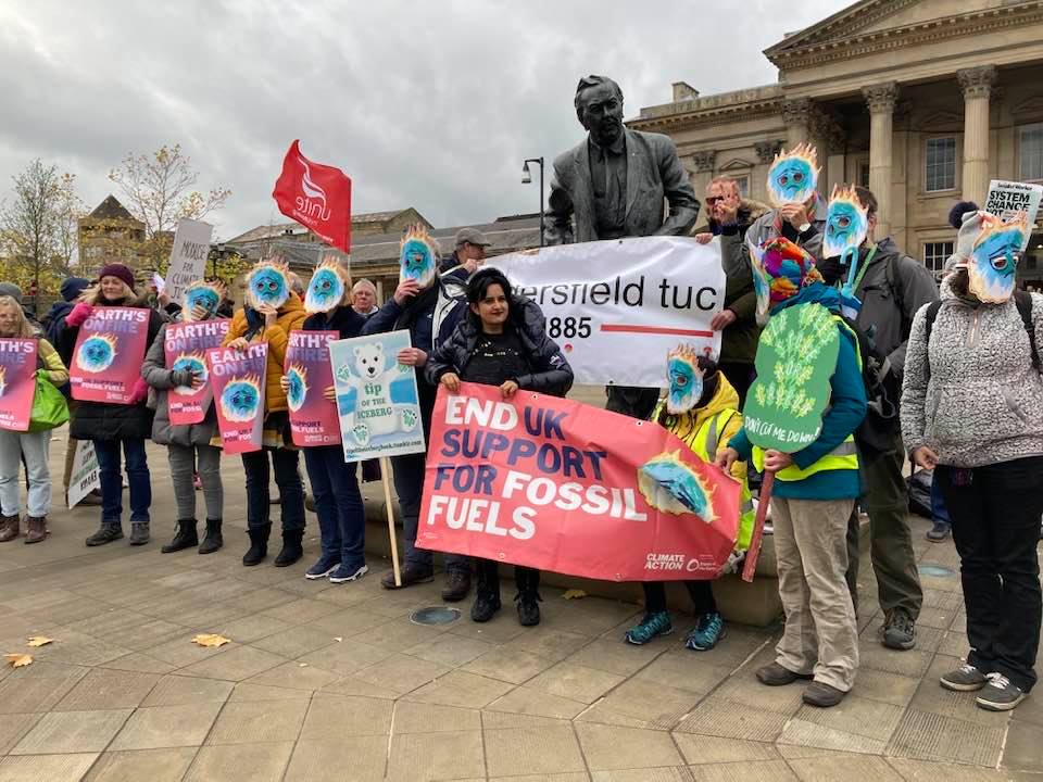 A group of people protesting - they're wearing colourful earth masks and holding a banner which reads "End UK support for fossil fuels"